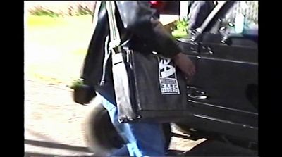 a man carrying a black bag walking past a car