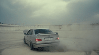 a silver car driving through a parking lot on a cloudy day