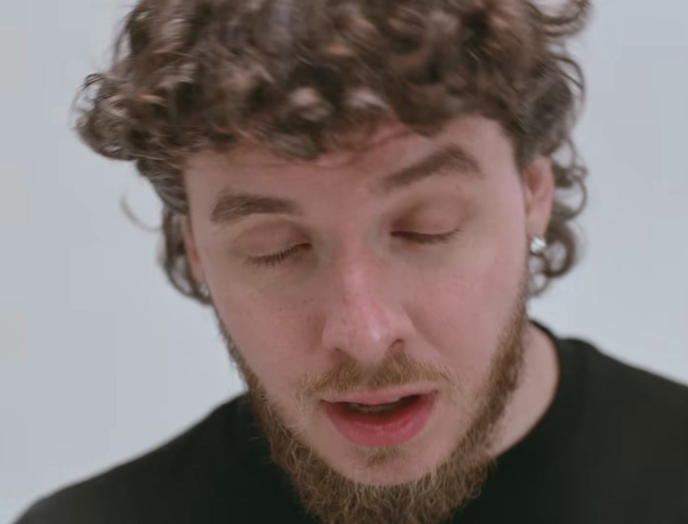 a man with curly hair is looking down at his cell phone