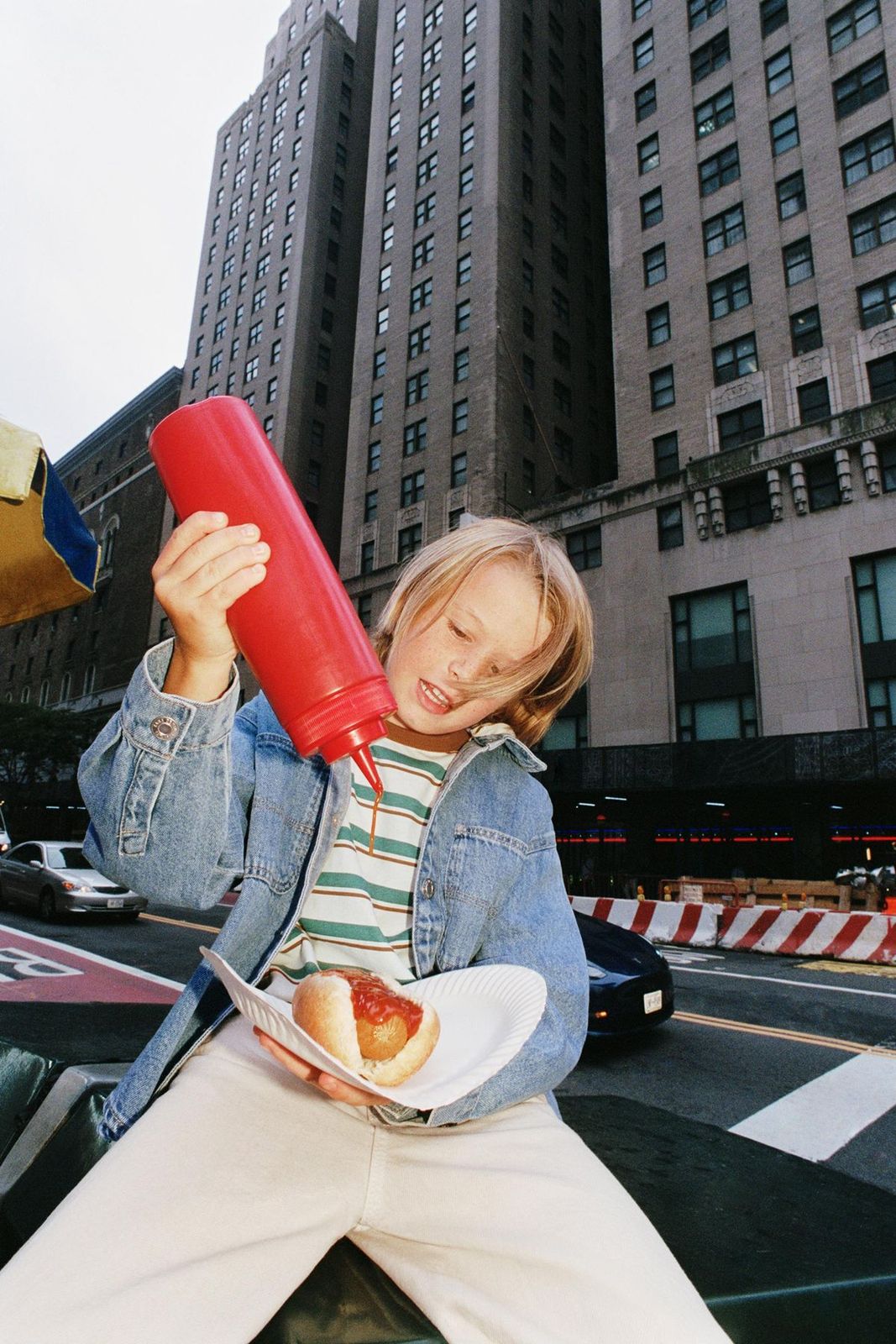 a little girl sitting on a curb eating a hot dog