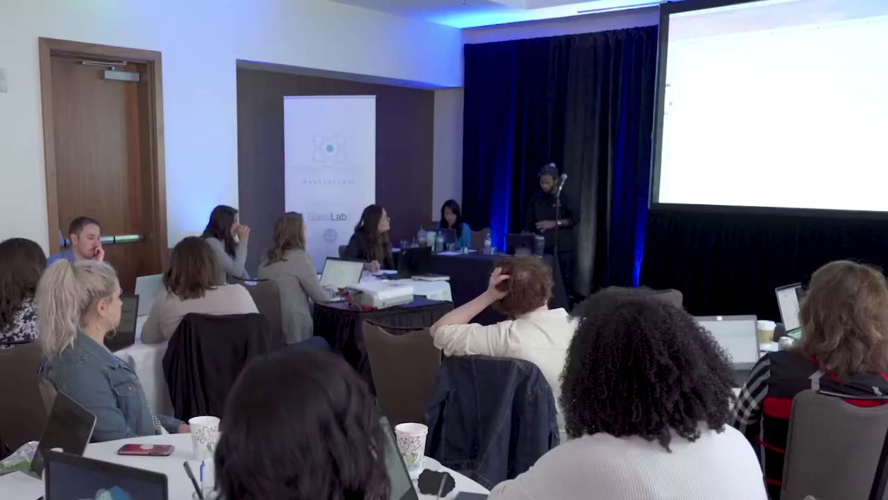 a group of people sitting at tables in front of a projector screen