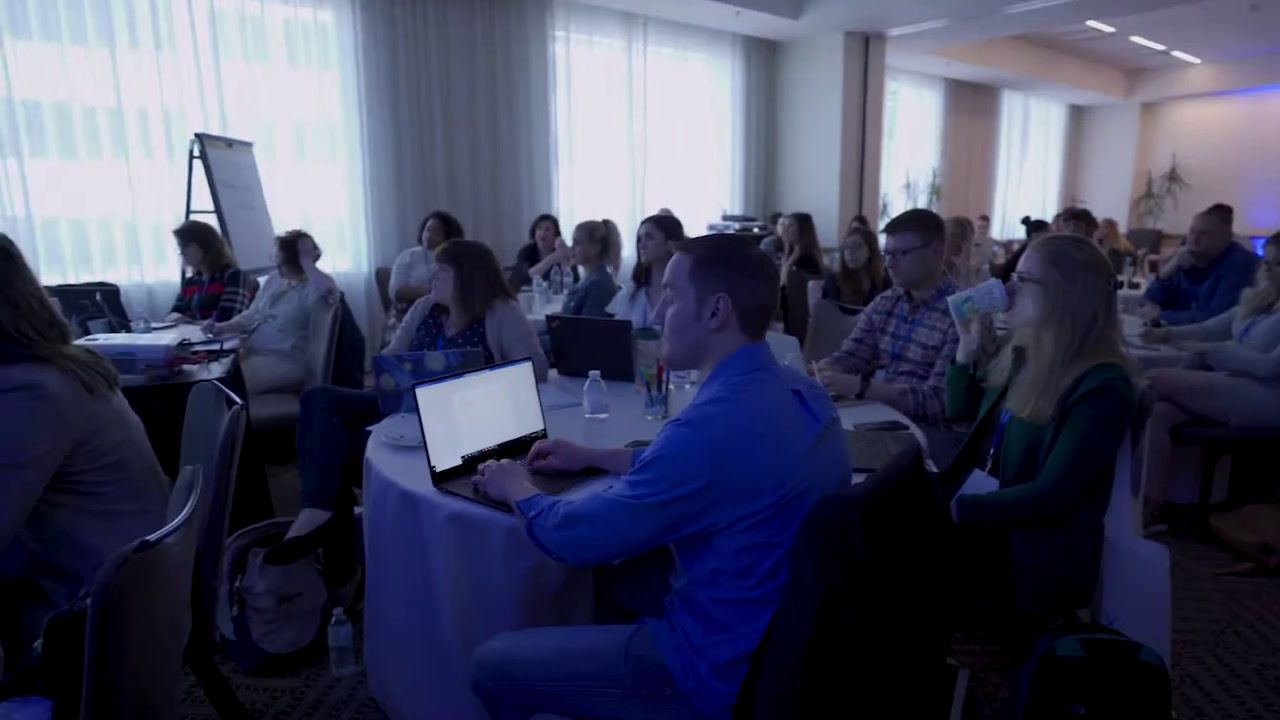 a group of people sitting around tables with laptops