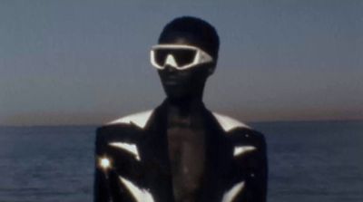 a man in a black and white suit standing in front of the ocean