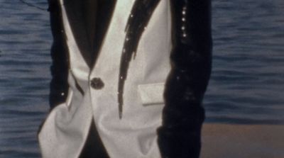 a man wearing a white and black suit standing next to a body of water