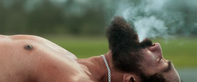 a shirtless man with a chain around his neck smoking a cigarette