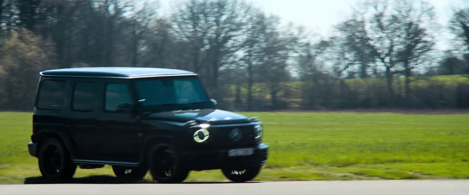 a black suv driving down a road next to a lush green field