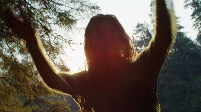 a woman standing in front of a tree with her arms in the air