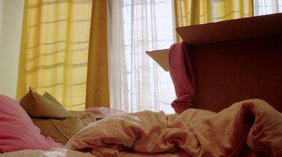 an unmade bed with a pink comforter and yellow curtains