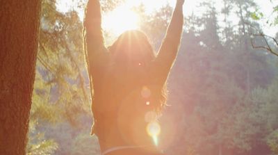 a woman standing in front of a tree with her arms in the air