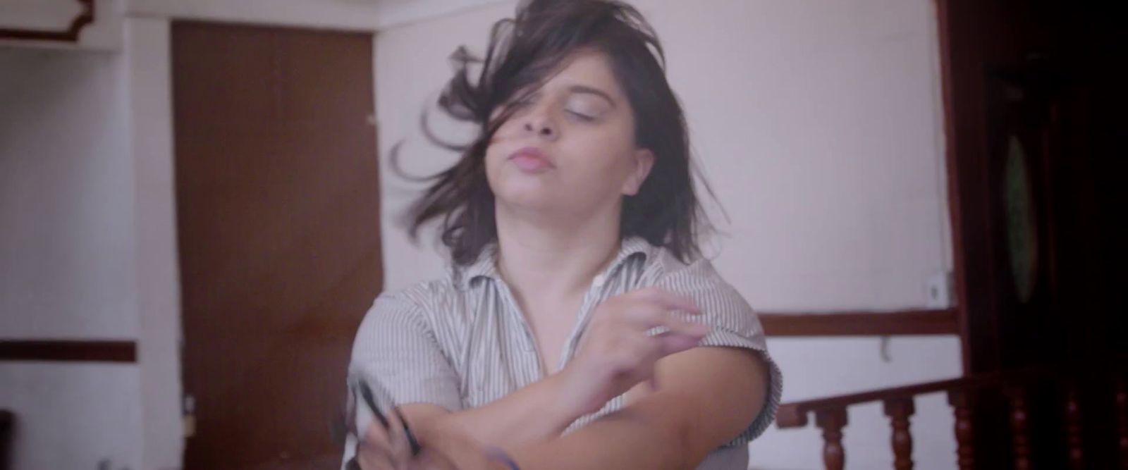 a woman standing in a room with her hair blowing in the wind