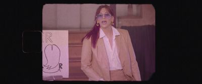 a woman with red hair and glasses standing in front of a sign