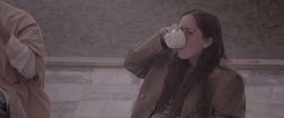 a woman drinking from a cup while standing next to a man