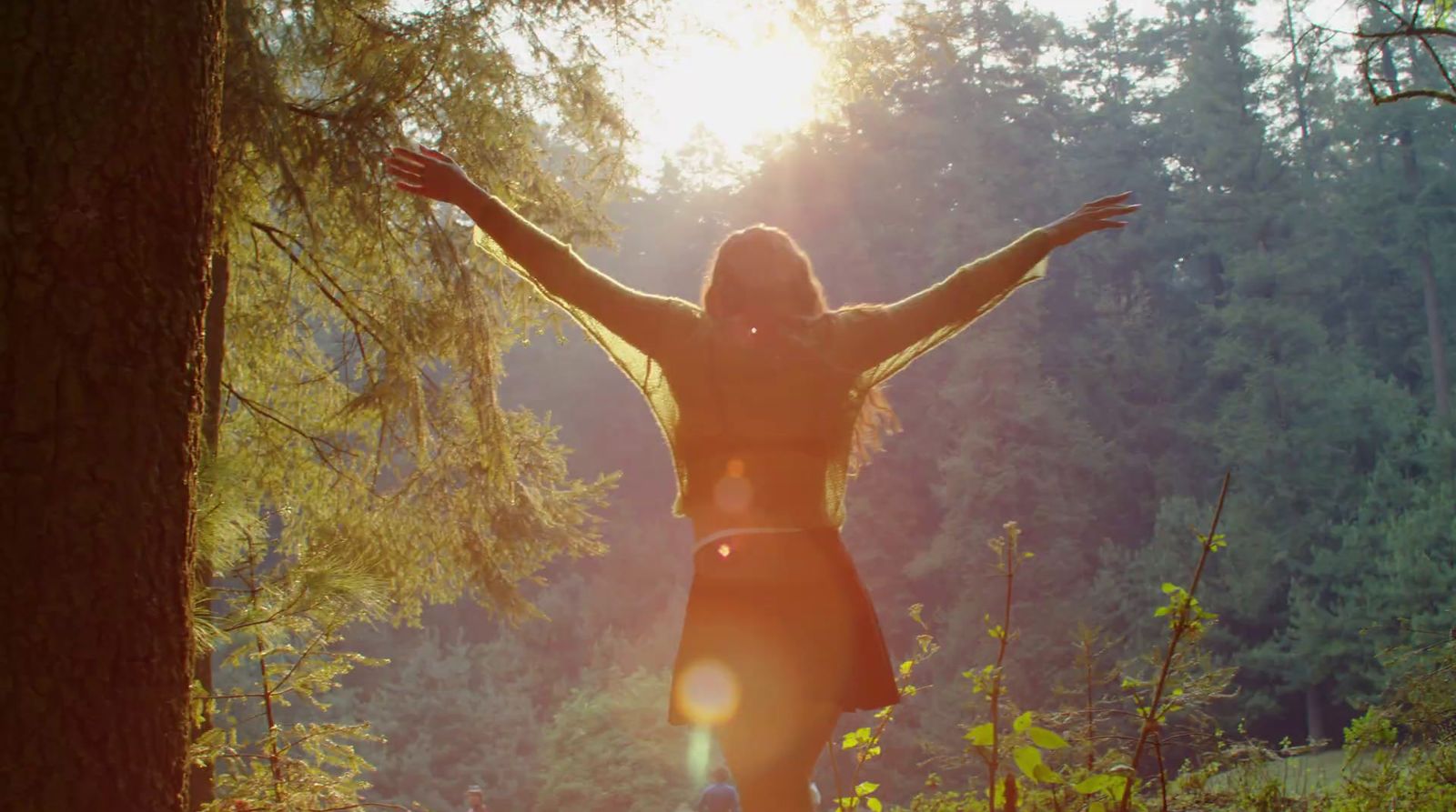 a woman standing in a forest with her arms outstretched