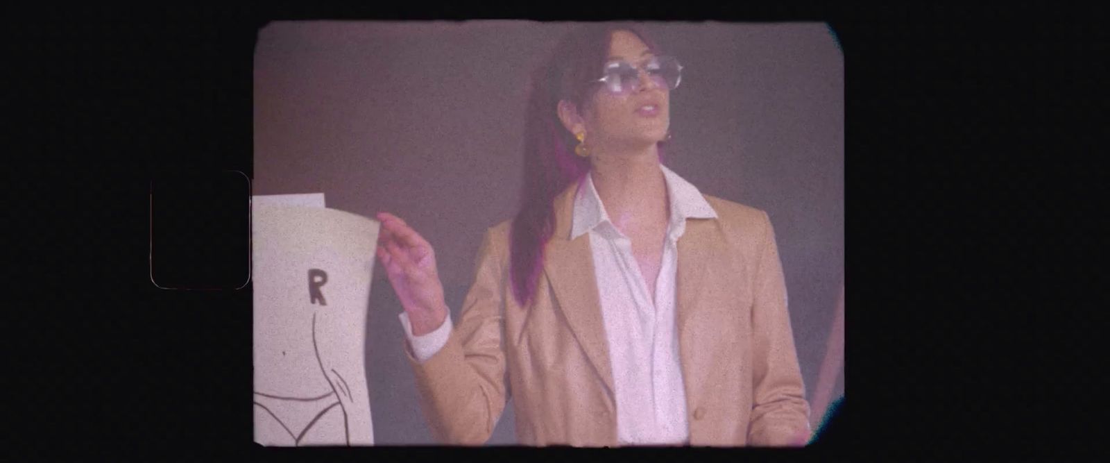 a woman in a suit and glasses standing in front of a black background