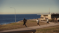 a group of people running on a path near the ocean