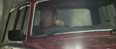 a man sitting in a red truck with his hand on the steering wheel