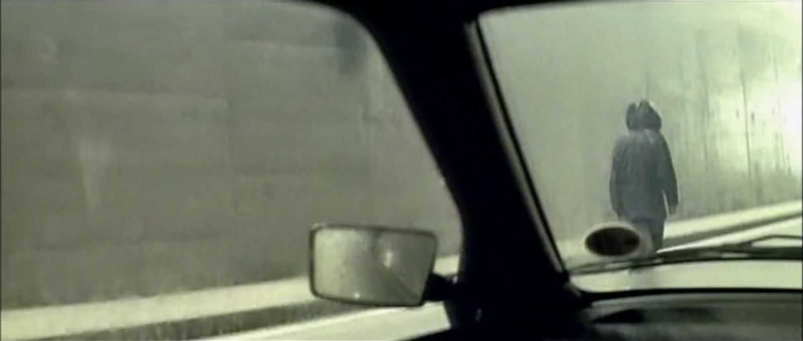 a rear view mirror of a car with a person walking in the rain