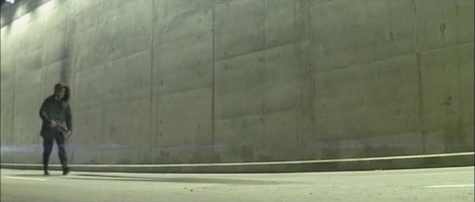 a woman walking down a street next to a wall