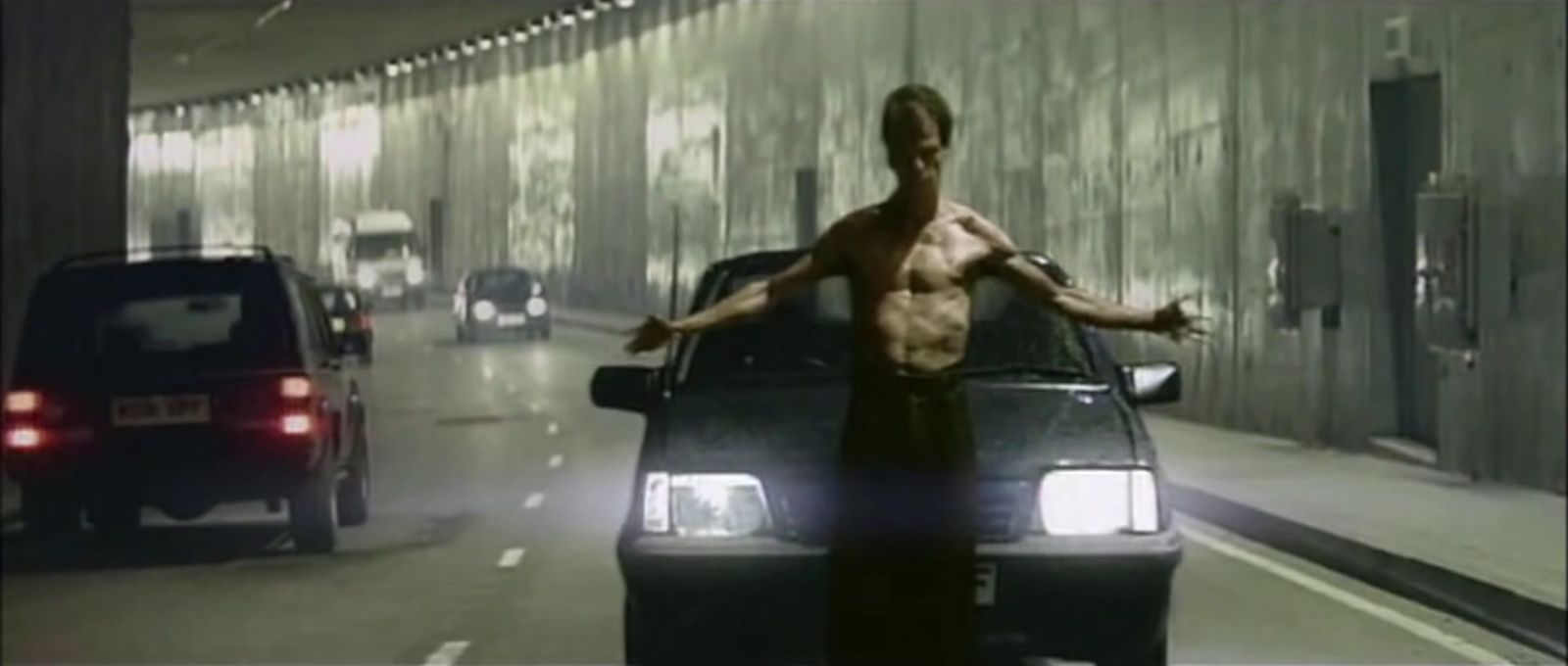 a shirtless man standing on the hood of a car