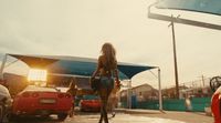 a woman walking across a parking lot next to a red car