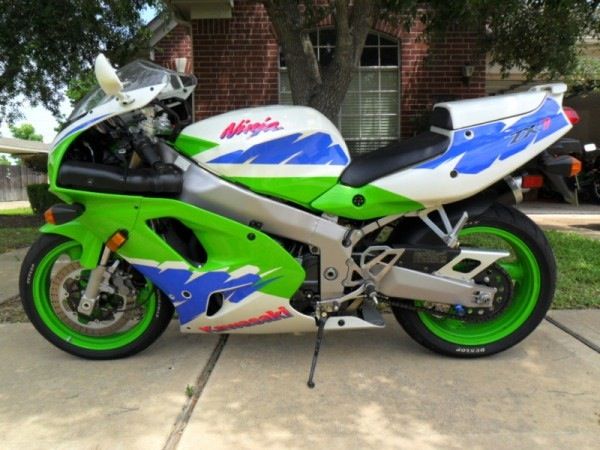 a green, white and blue motorcycle parked in front of a house