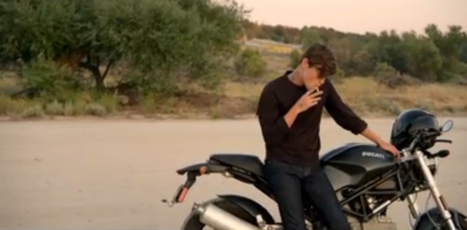 a man sitting on a motorcycle smoking a cigarette