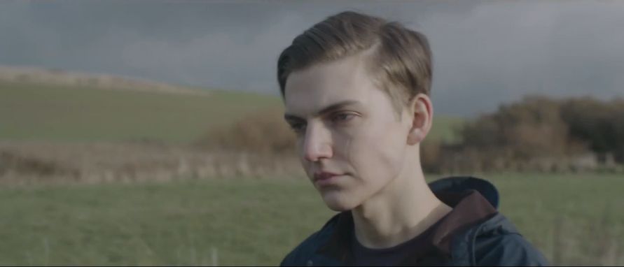 a man standing in a field with a cloudy sky in the background