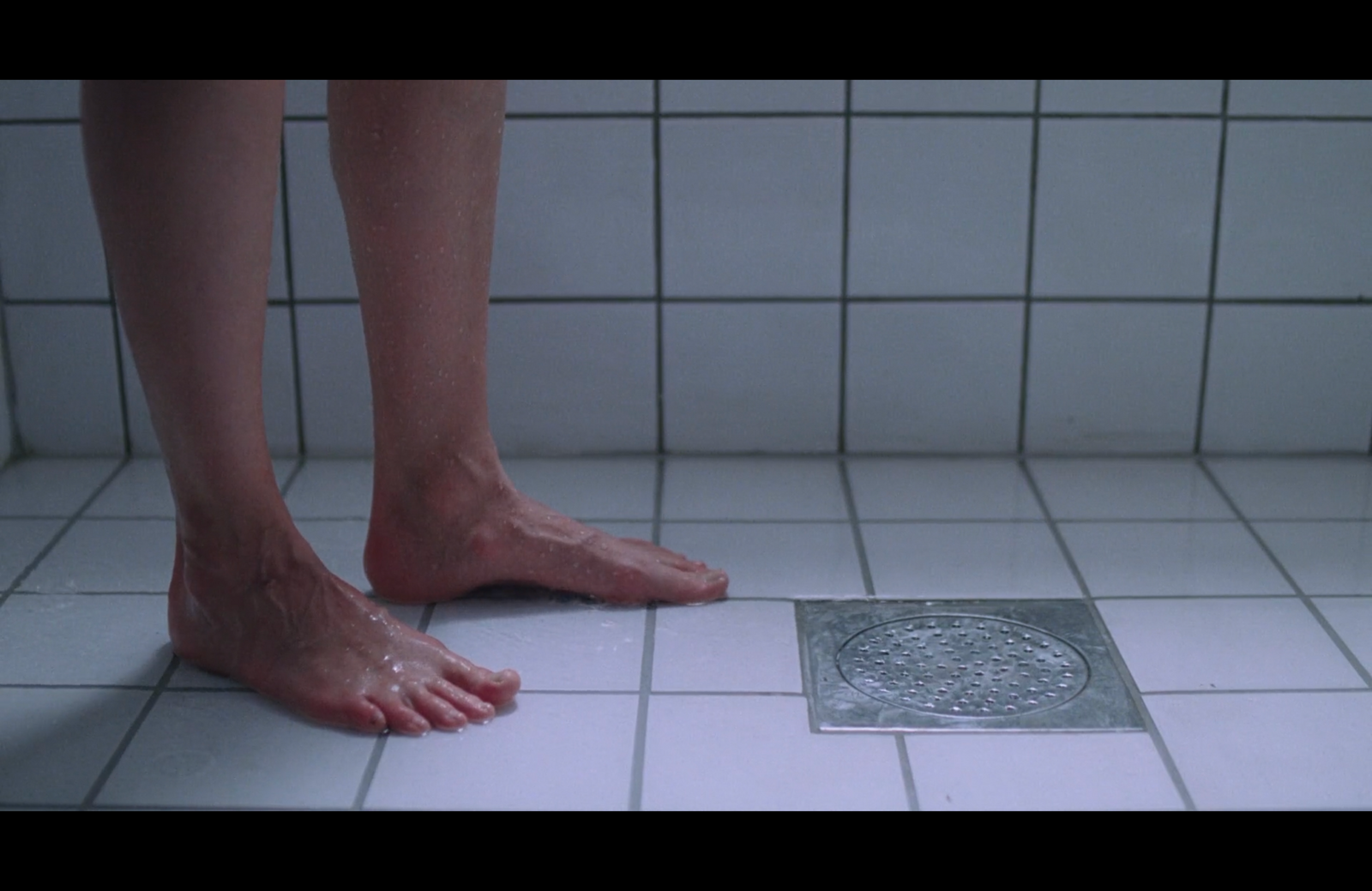 a person standing on a bathroom floor next to a drain