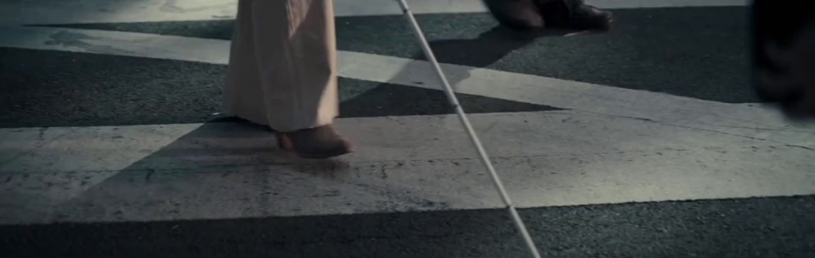 a person walking across a cross walk with a cane