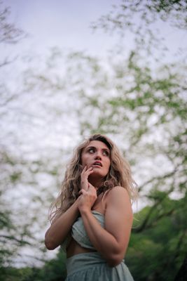 a woman standing in front of a tree with her hand under her chin