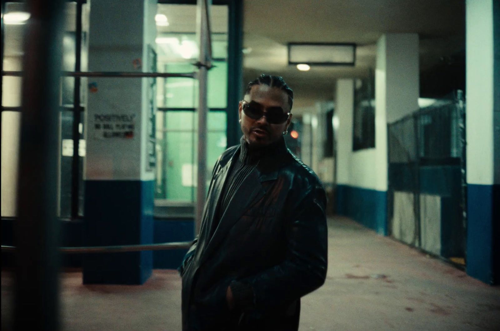 a man in a black jacket and sunglasses standing in a hallway