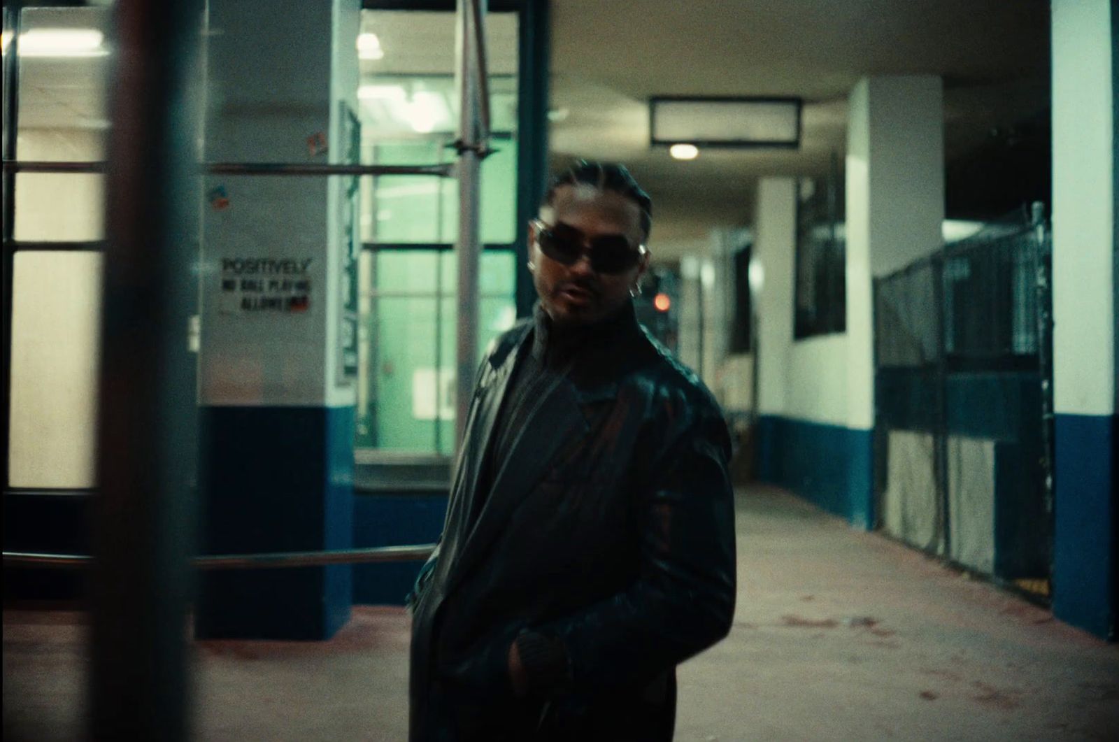 a man in a black jacket and sunglasses standing in a hallway