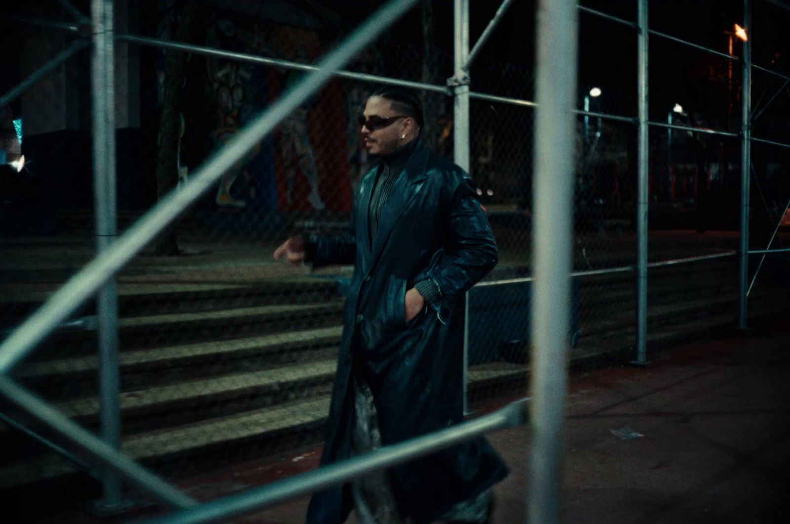 a man in a black coat and sunglasses walking down a street