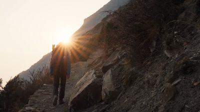 a man walking up a mountain trail at sunset