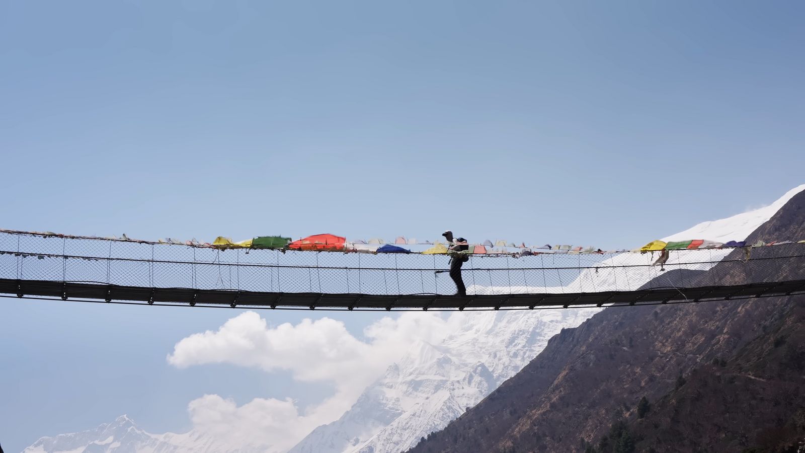 a man walking across a suspension bridge over a mountain