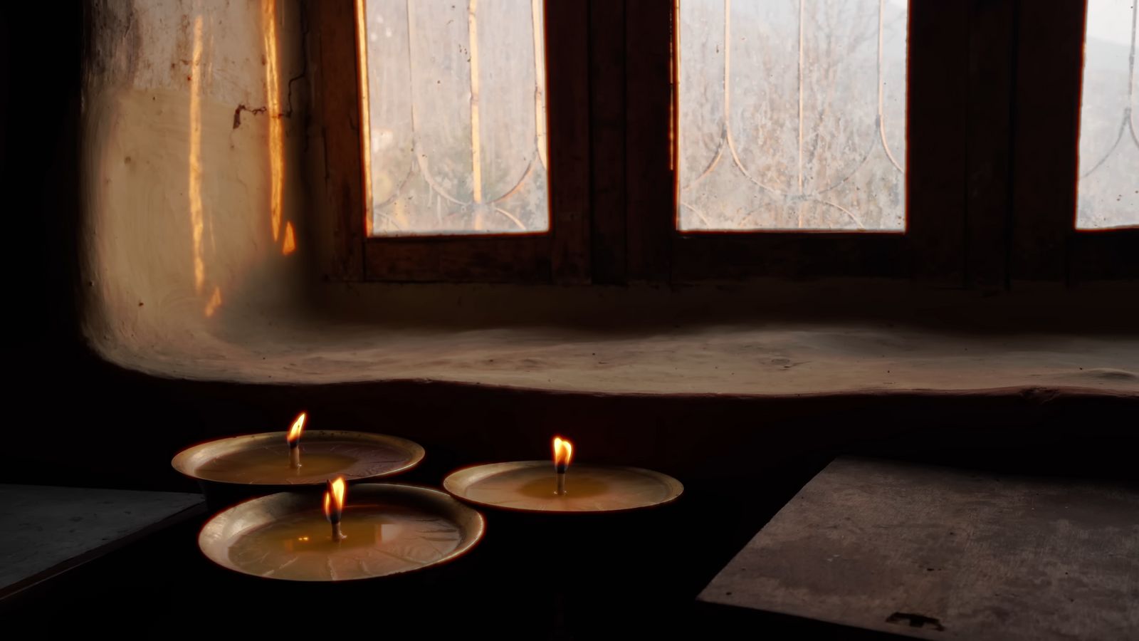 three lit candles sitting in front of a window