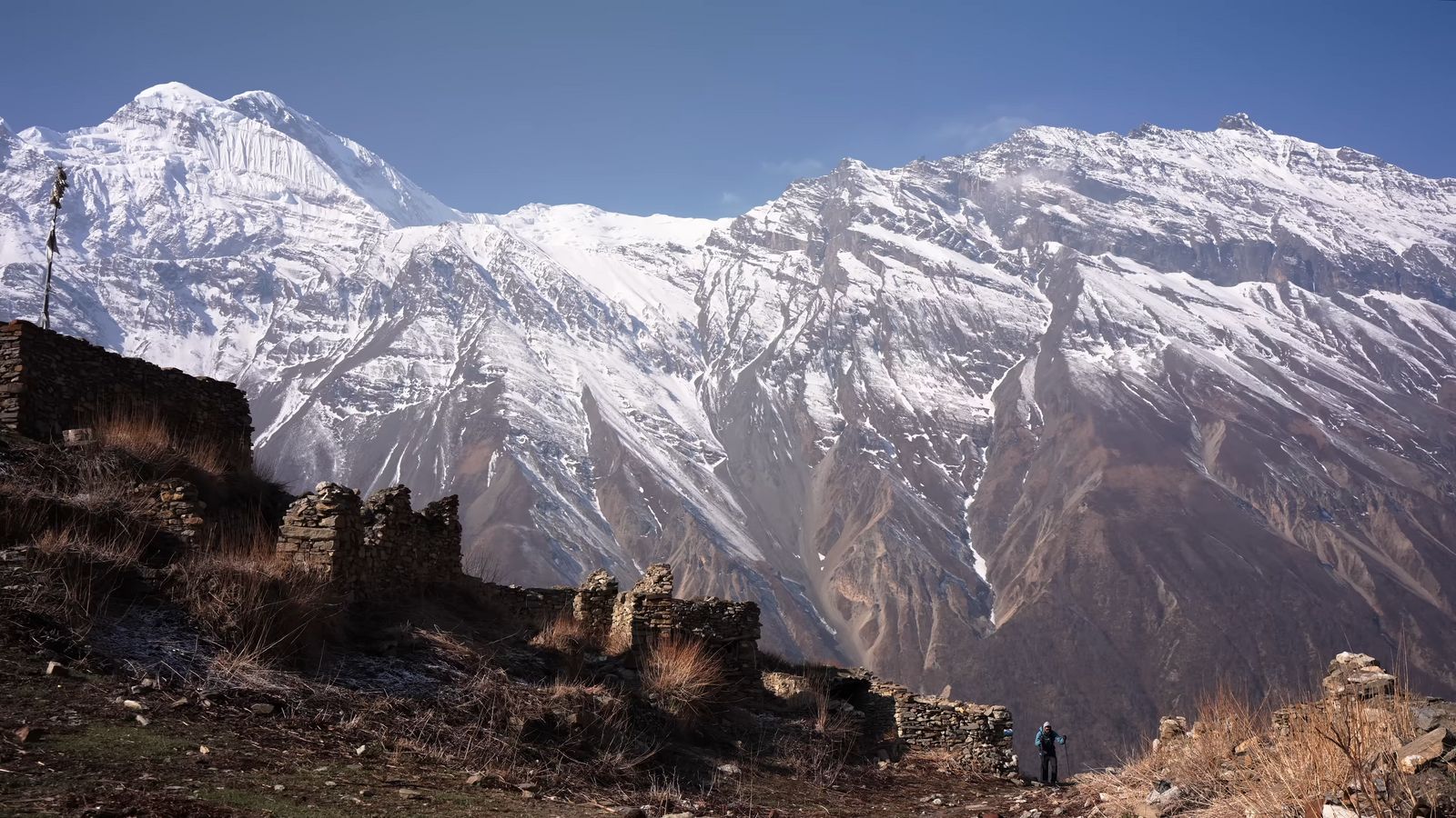 a snow covered mountain range with a person standing on a hill