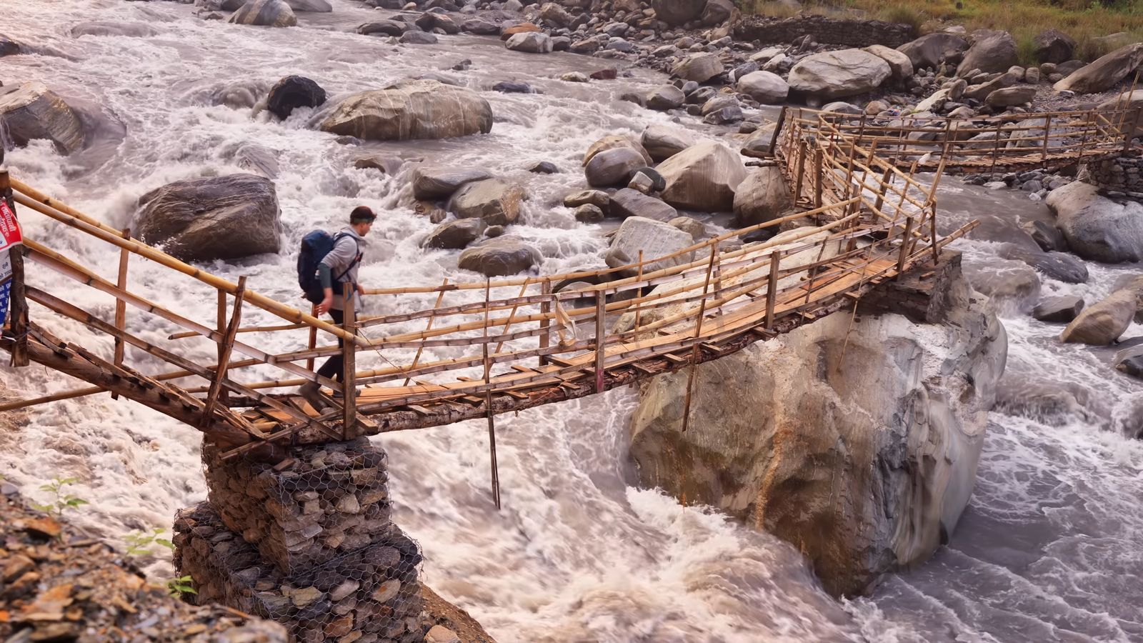 two people crossing a wooden bridge over a river