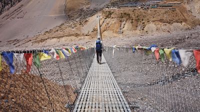 a man walking across a suspension bridge over a river