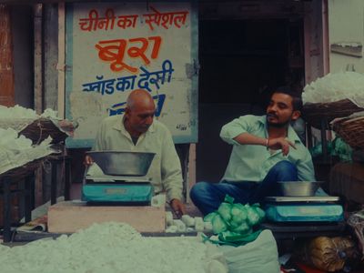 two men sitting in front of a store selling food