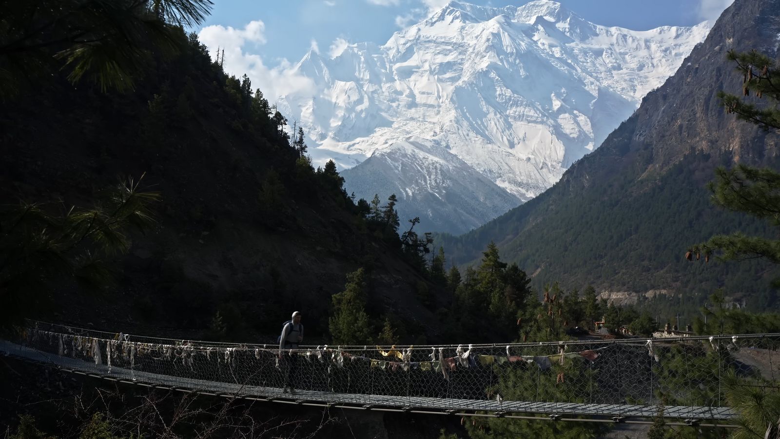 a man walking across a suspension bridge in the mountains