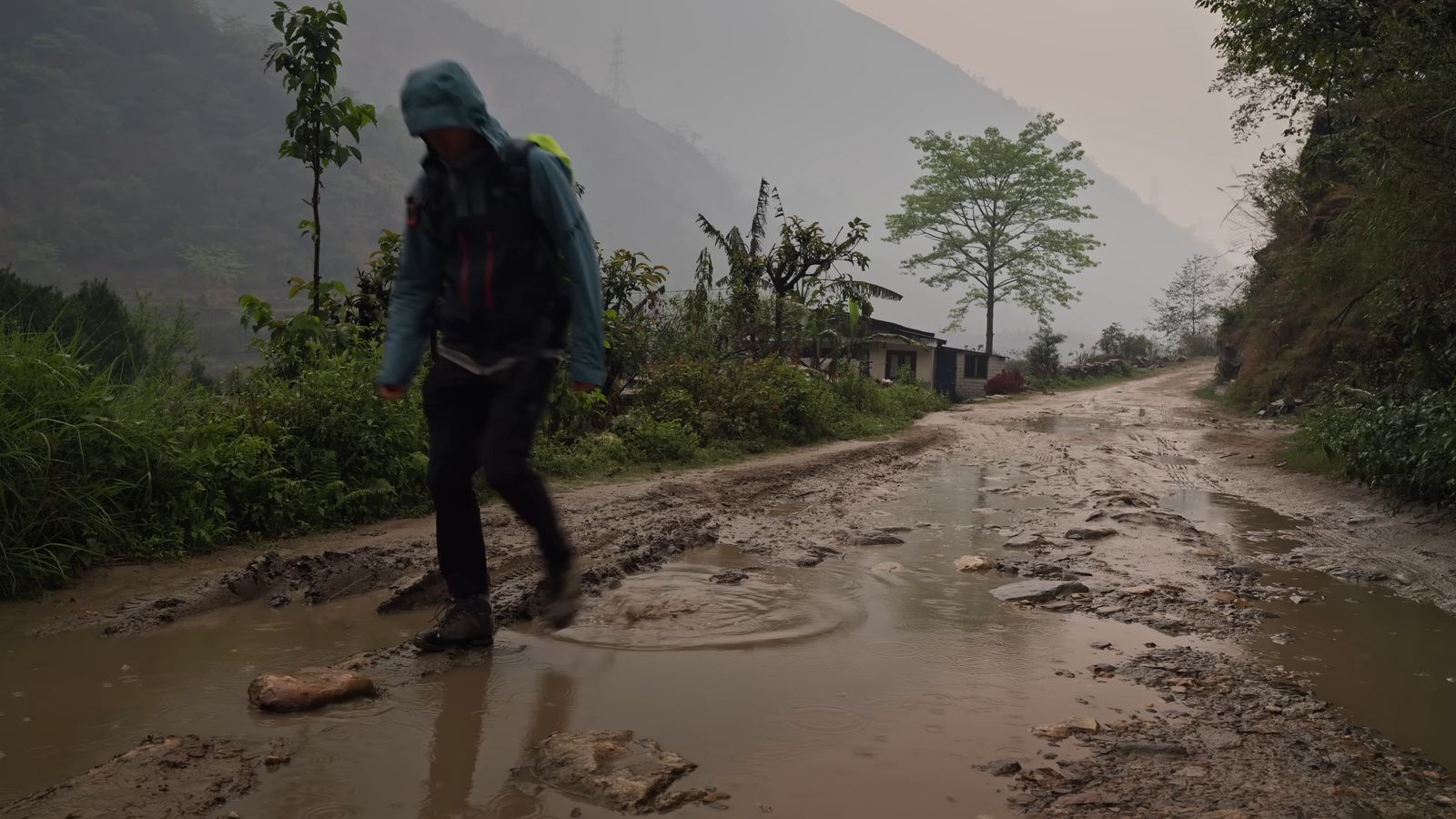 a man walking across a muddy road in the rain