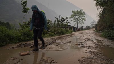 a man walking across a muddy road in the rain