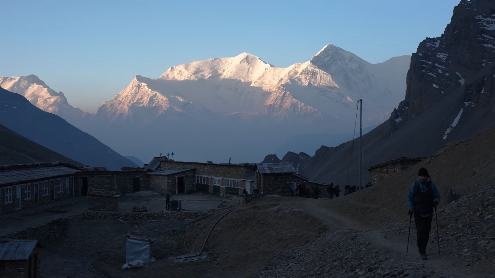 a person walking up a dirt road with mountains in the background