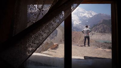 a man standing in front of a window with mountains in the background