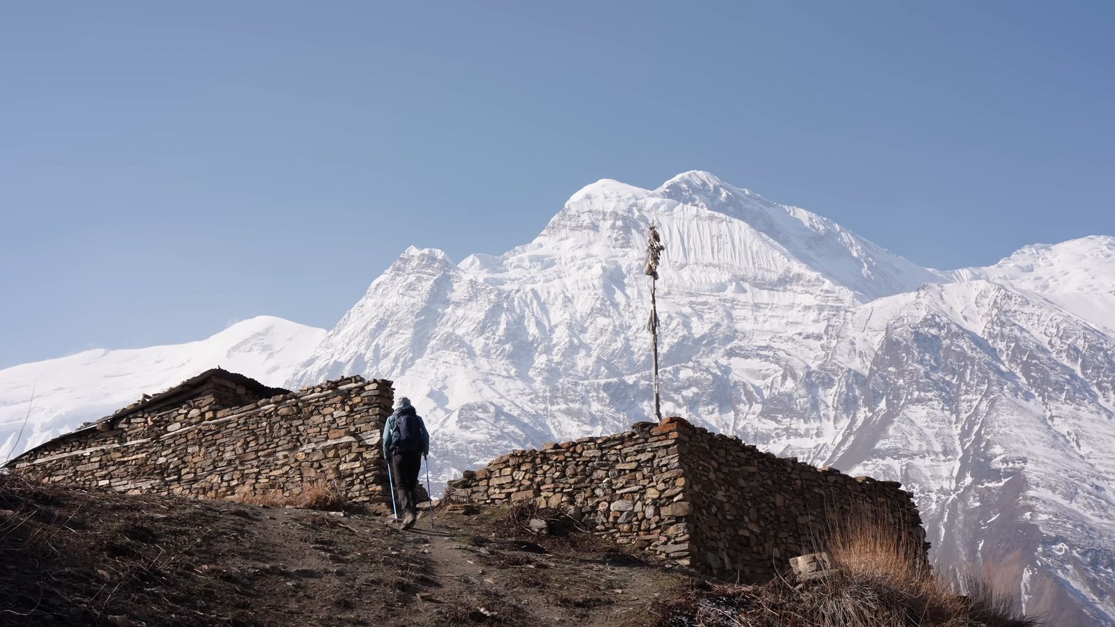 a man standing on top of a mountain next to a stone wall