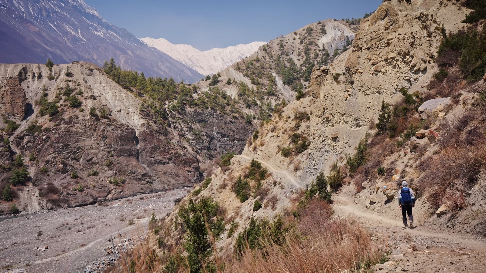 a man walking down a dirt road next to a mountain