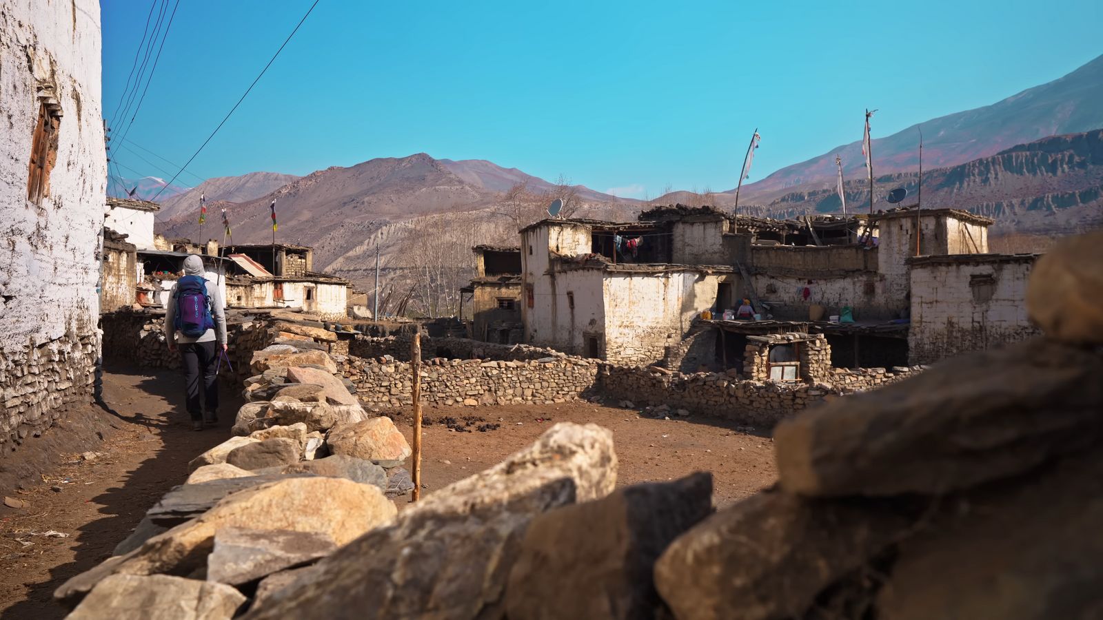 a man walking down a dirt road next to a stone wall