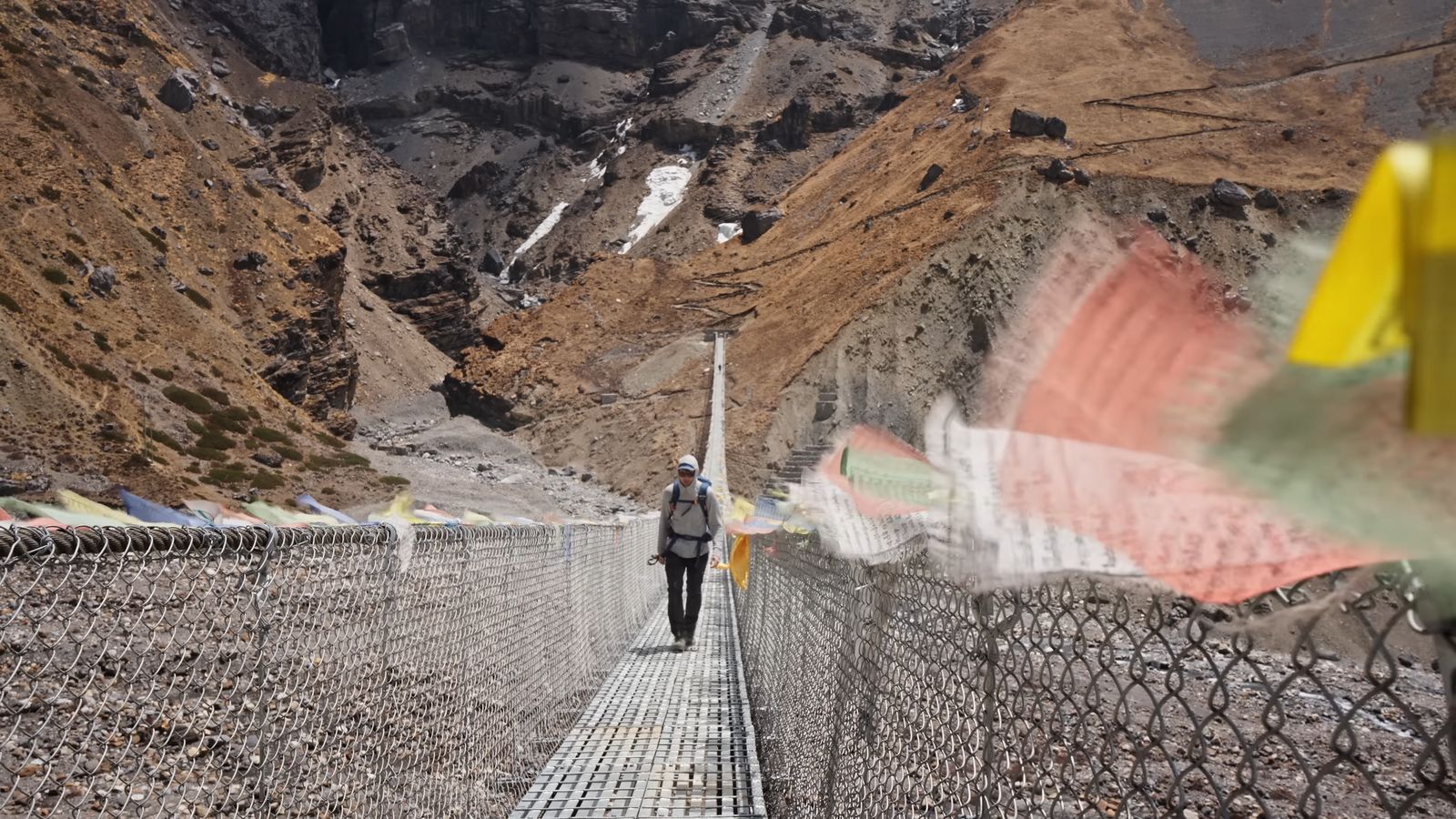 a man walking across a suspension bridge in the mountains