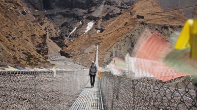 a man walking across a suspension bridge in the mountains